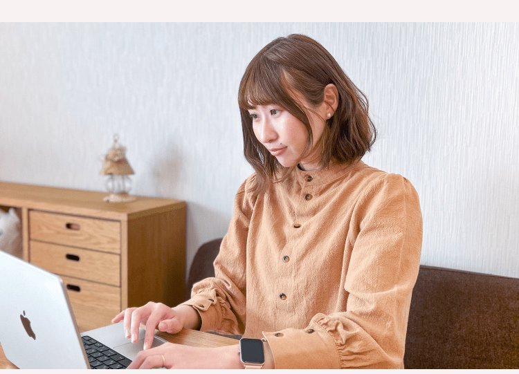 木製の棚の前でノートパソコンを操作する、キャメルシャツの女性