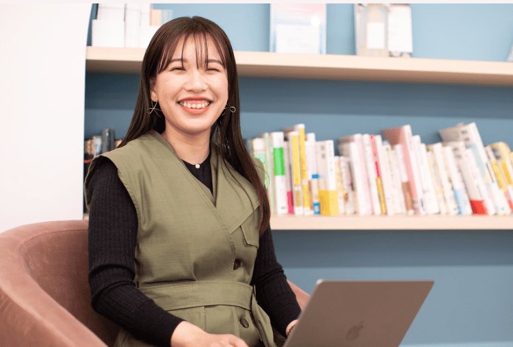 本棚を背に、ノートPCを操作しながら微笑む女性
