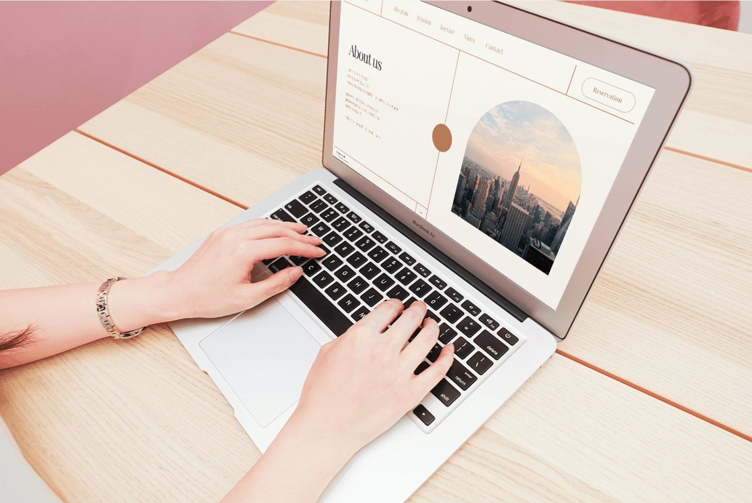 木のテーブルでノートパソコンを操作しながらWebサイトを制作している手元