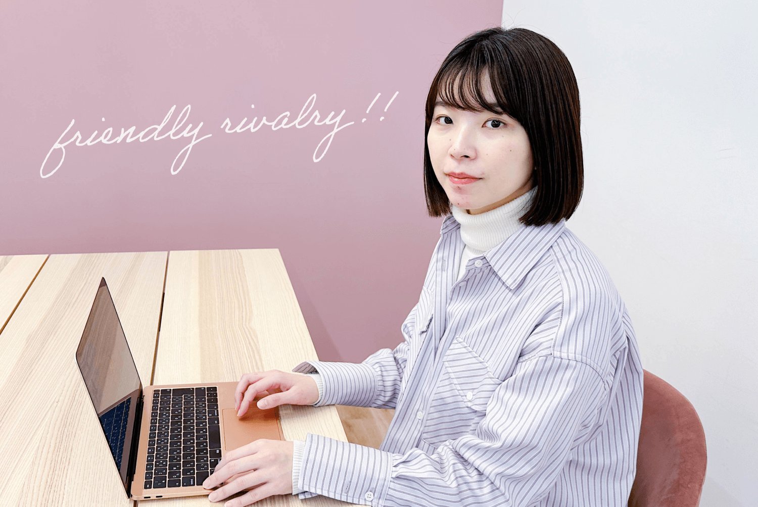 くすんだピンクの壁に「friendly rivalry!!」の手書き文字。こちらを見て微笑む女性