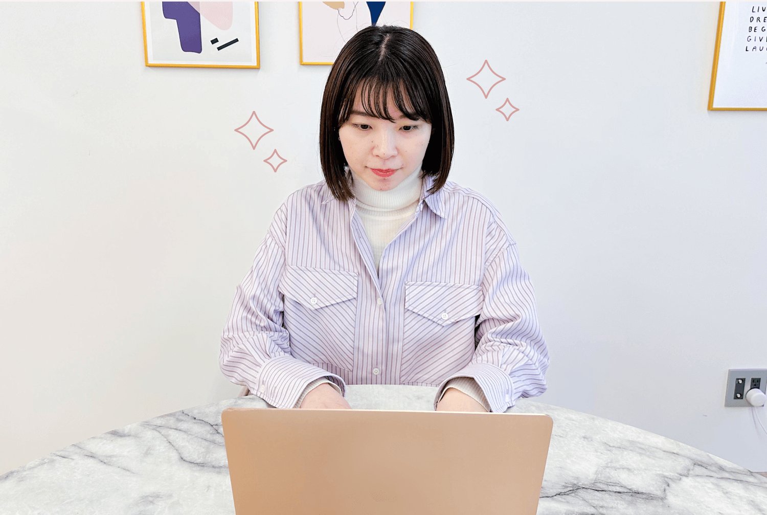 白い壁にアートフレームが並ぶ室内。キラキラの装飾入りで、正面を向いて座る女性