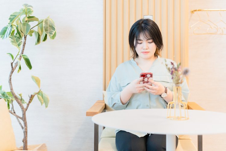 カフェのような店内で椅子に座り、スマートフォンを見つめるゆかりさん