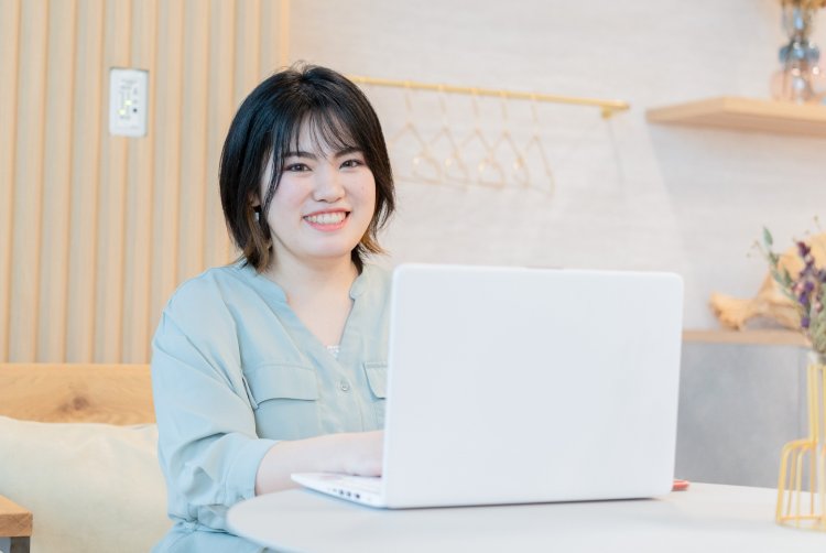 ハンガーラックのある部屋でノートパソコンに向かい微笑むゆかりさん