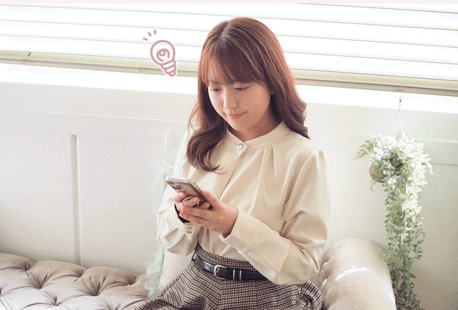 窓辺のソファに座り、スマートフォンを見て微笑む女性