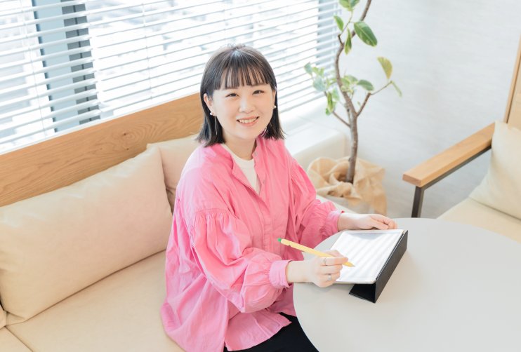 窓際のソファに座り、手元のノートにペンで書き込みながら微笑むkahoさん