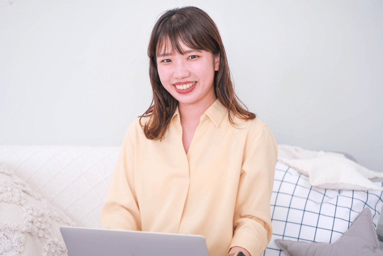 ベッドの上でノートパソコンを操作しながら微笑む女性