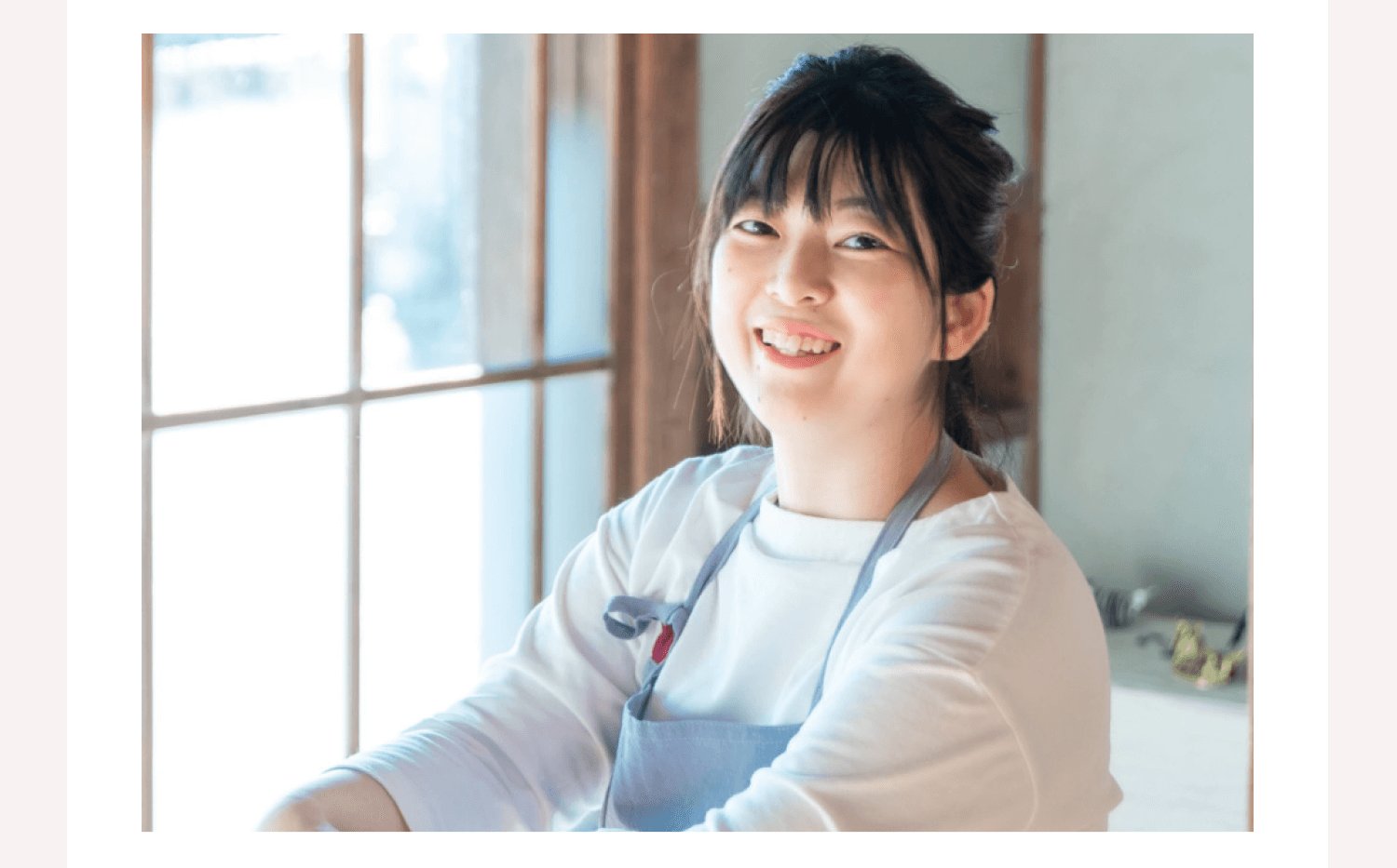 パートナーデザイナーのくみさんの胸から上のポートレート。古民家風の窓辺でエプロン姿で微笑んでいる