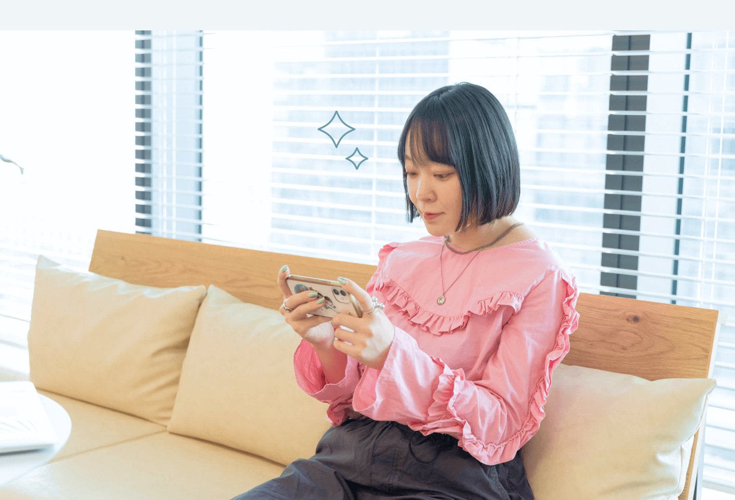 部屋のソファでスマホを操作する本人（ピンクブラウス）