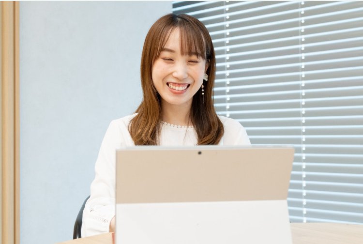 ブラインド越しの窓辺でノートPCに向かって笑う女性