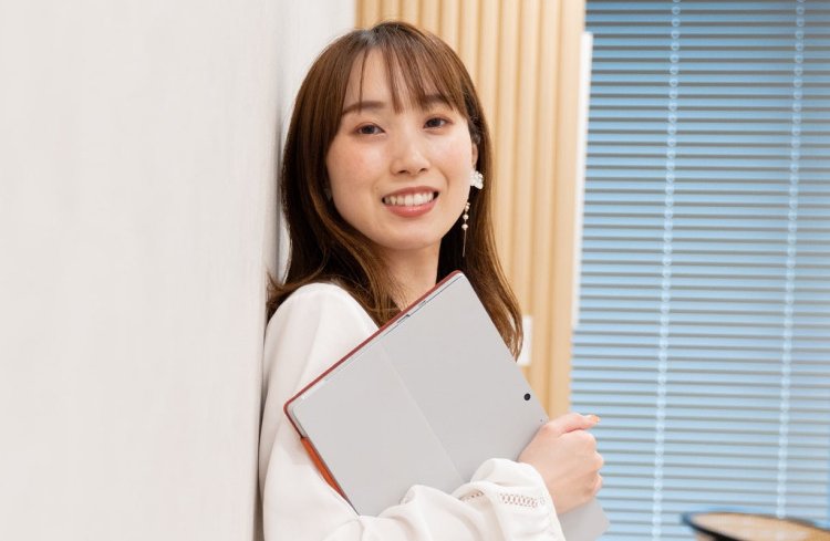廊下の壁に寄りかかりノートPCを抱えて微笑む女性