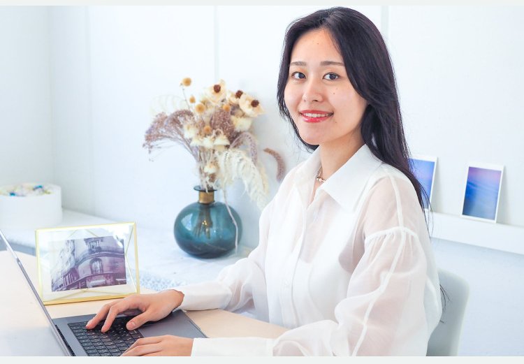 花瓶と写真立てのある部屋でノートPCに向かい微笑むパウさん