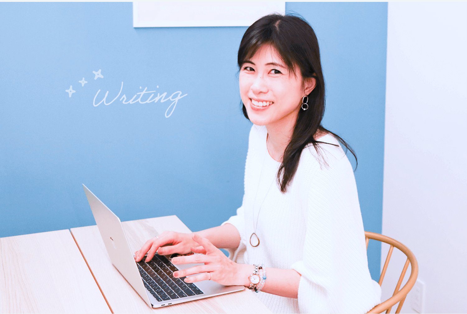 青い壁の前でノートPCをタイピングしながら微笑むsatominさん