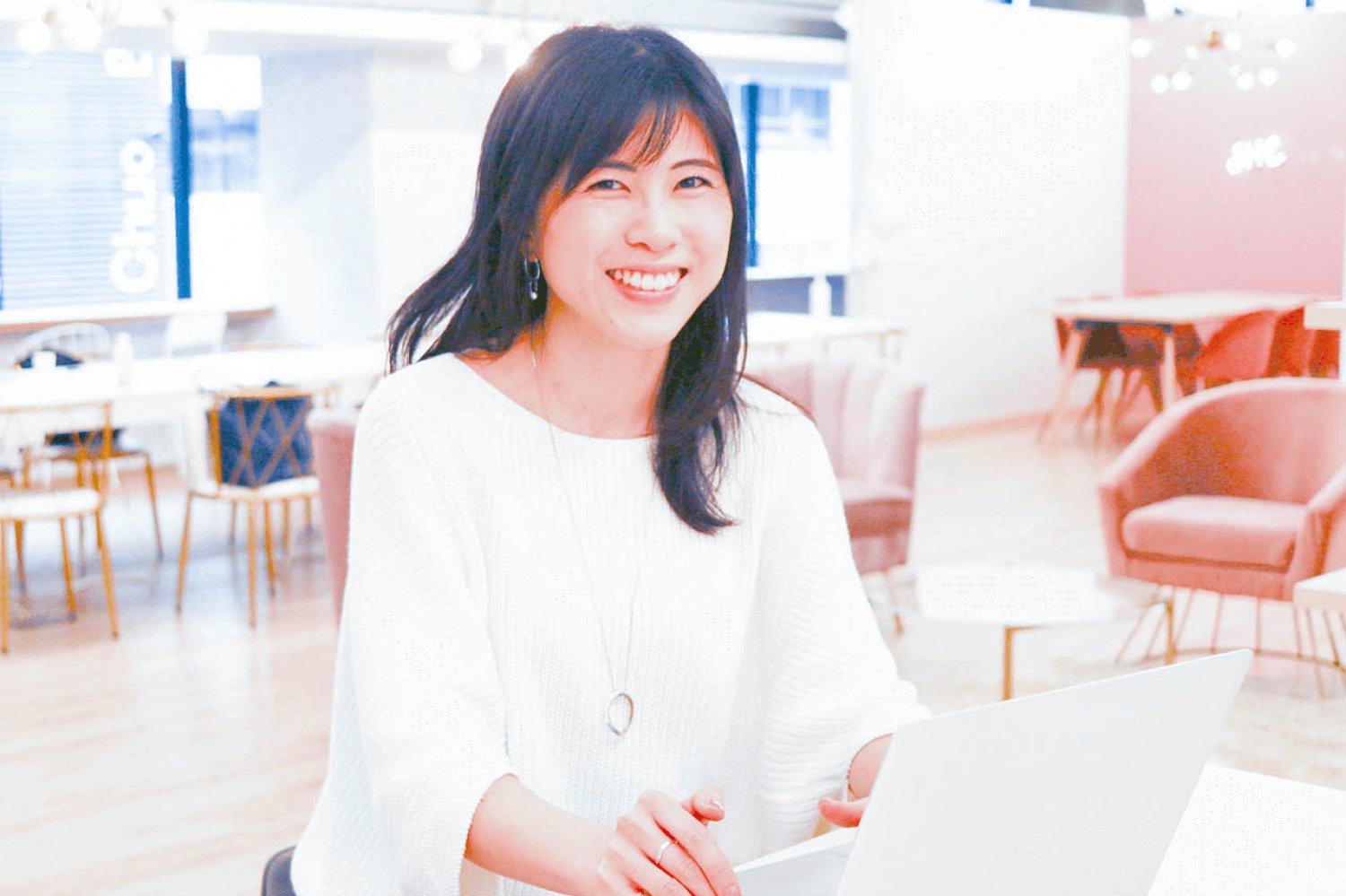 カフェラウンジに立ち、白いノートPCを持って微笑むsatominさん