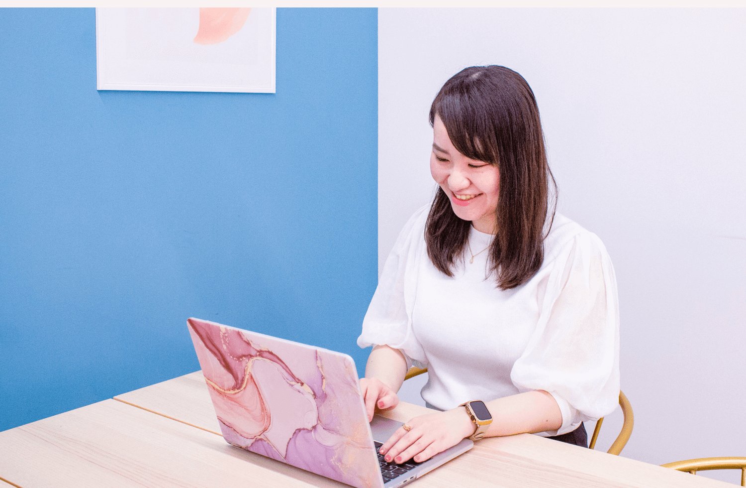 青い壁の部屋でノートPCに向かい微笑むぺちさんの上半身写真