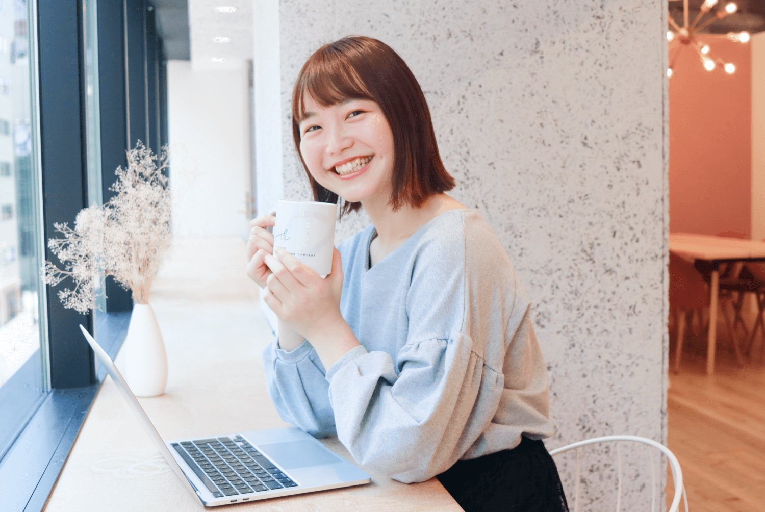 窓際でコーヒーマグを持ち微笑むHimawariさん