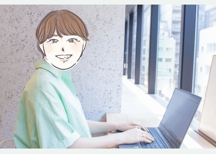 窓際のデスクでノートパソコンを操作するYANOさん。コンクリート壁と高層ビル群が見える大きな窓が背景