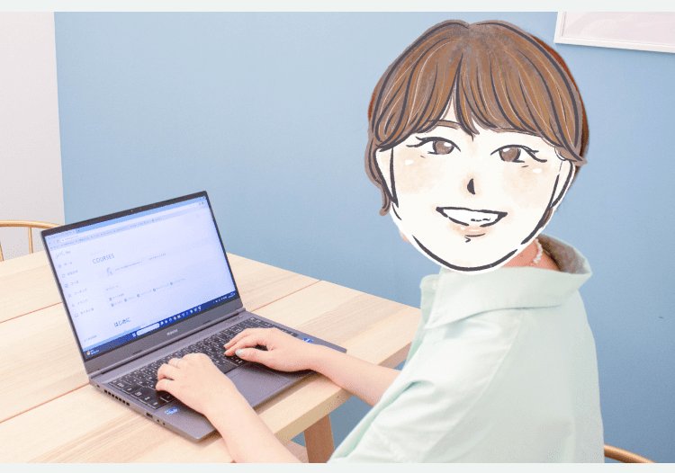 木製テーブルでノートパソコンを操作するYANOさん。背景は青い壁