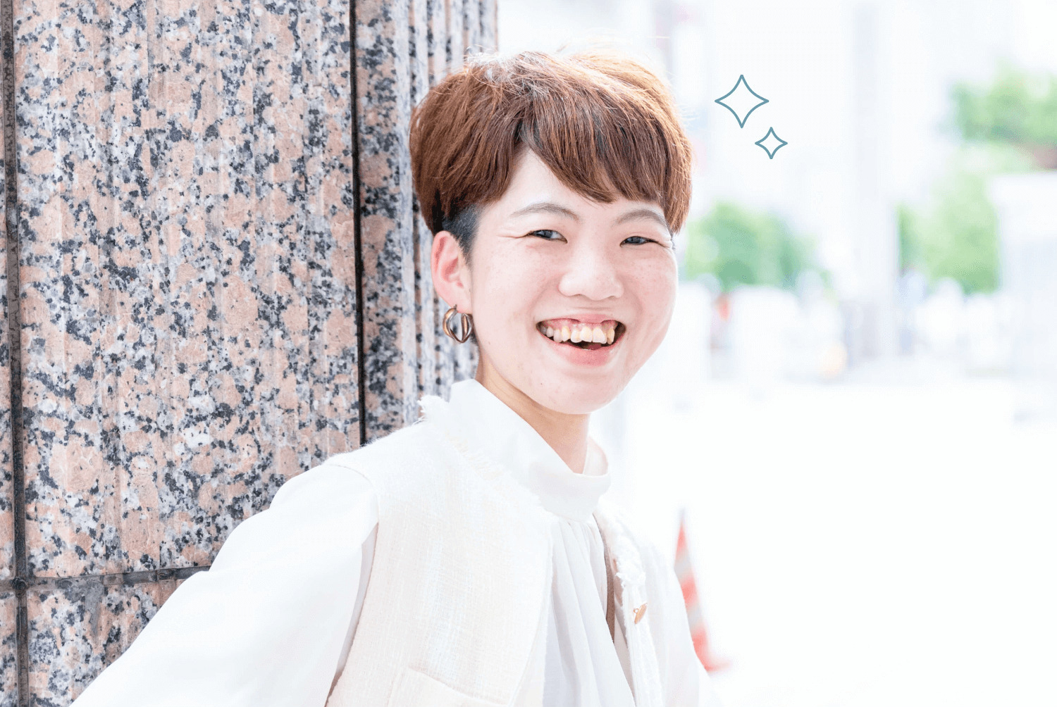 石造りの壁を背景に、はじけるような笑顔でこちらを見るSAYAKAさんの写真
