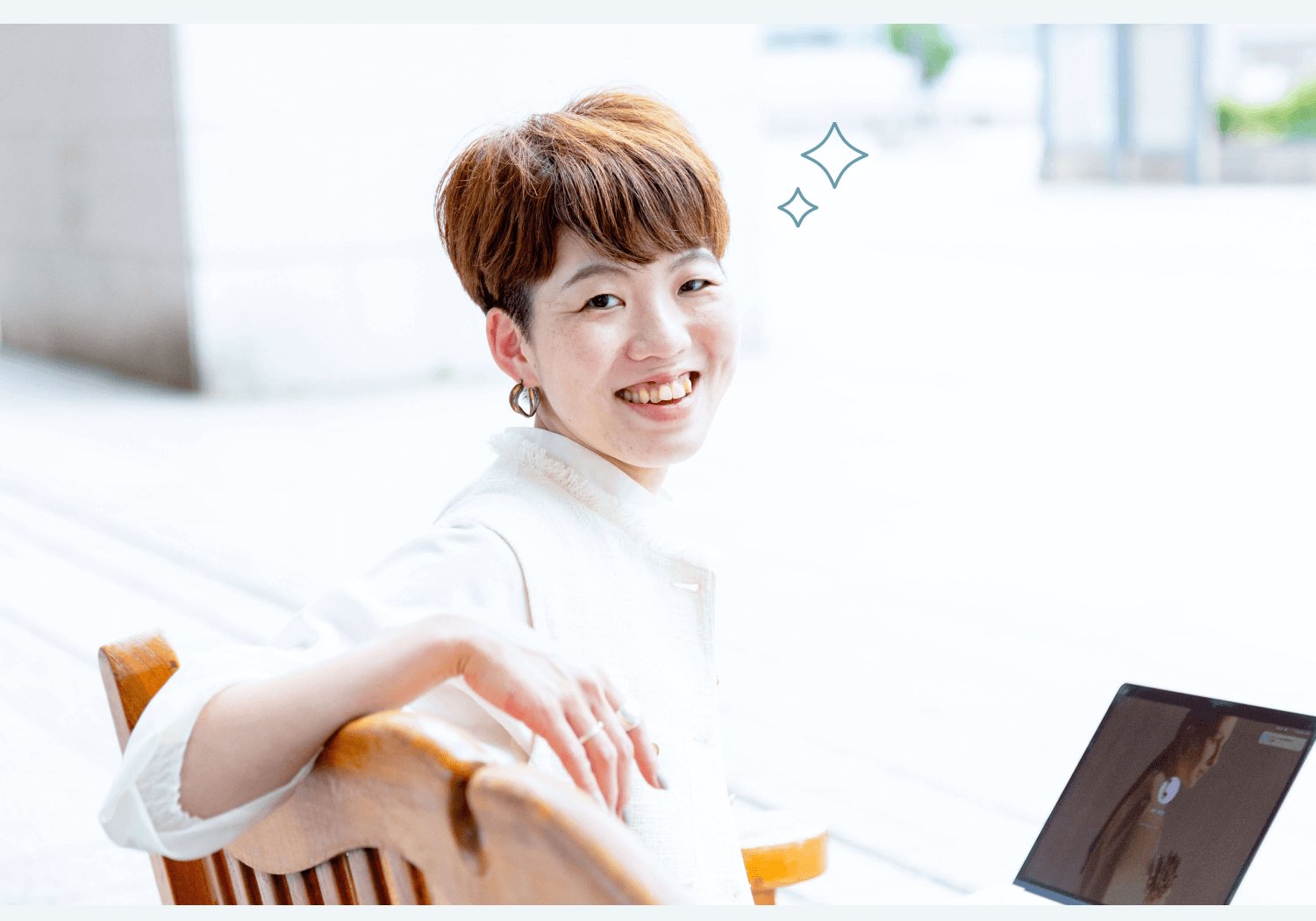 屋外で椅子に腰掛け、振り返って微笑むSAYAKAさんの写真