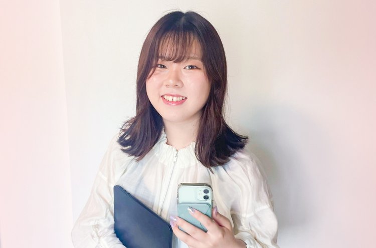 白ブラウス姿でノートPCとスマホを持ち微笑むナギさん