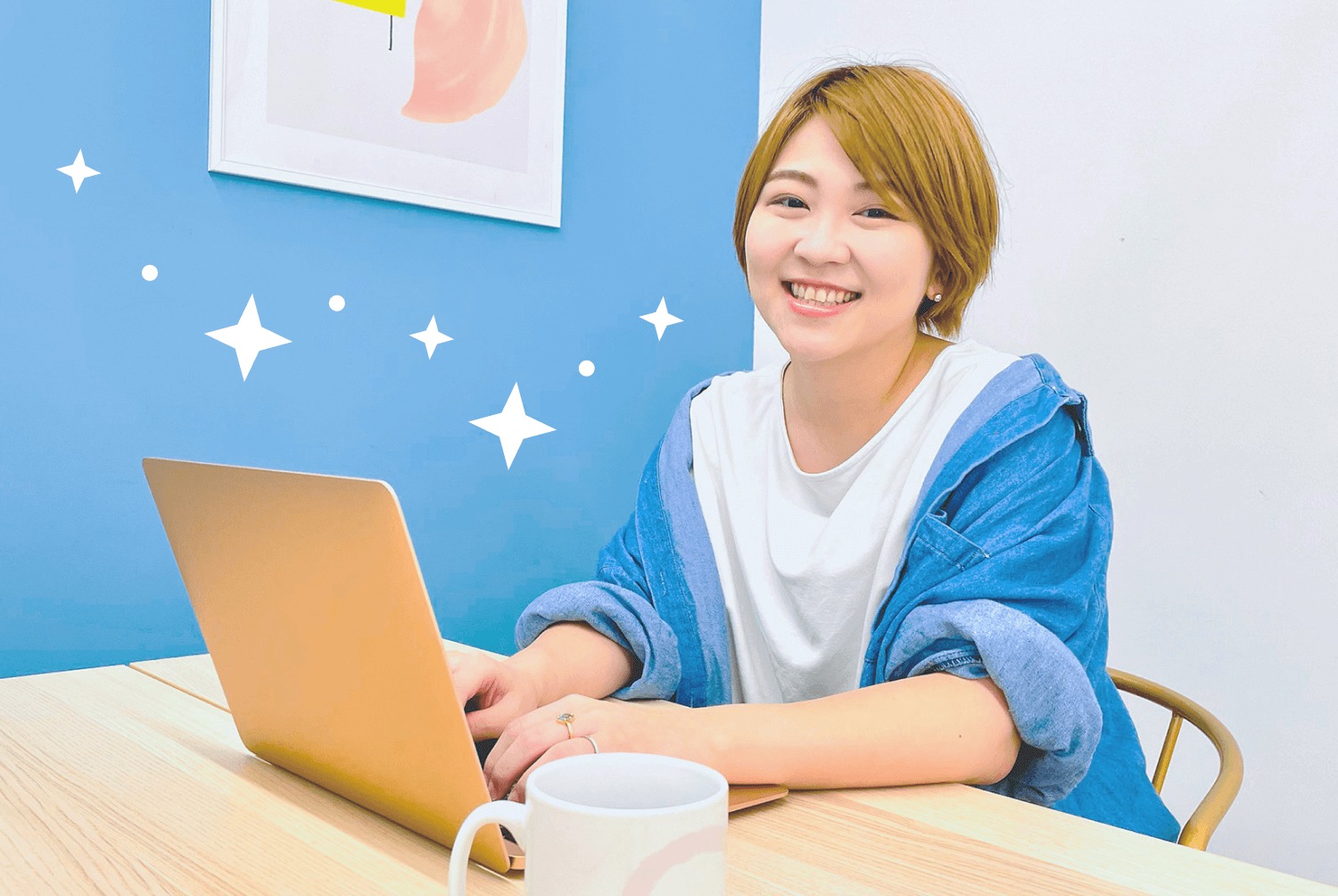 青い壁とスパークルの装飾を背景に、ノートパソコンに向かい微笑むなりーさん