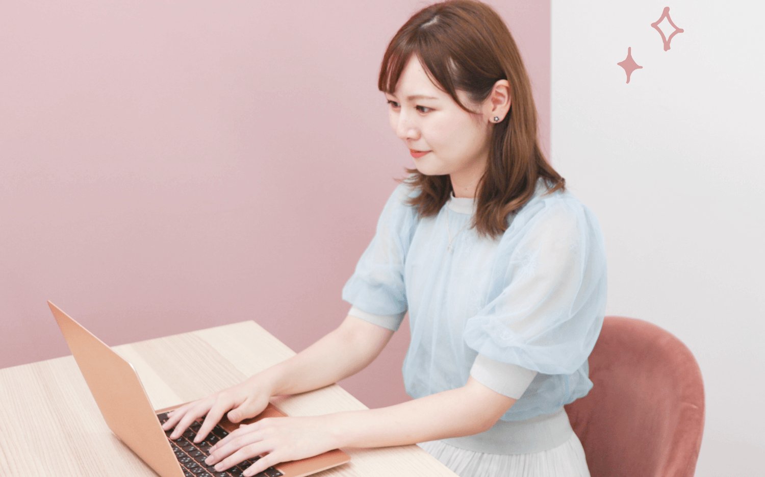 ピンクの壁の前でノートPCを操作する琴弓さん