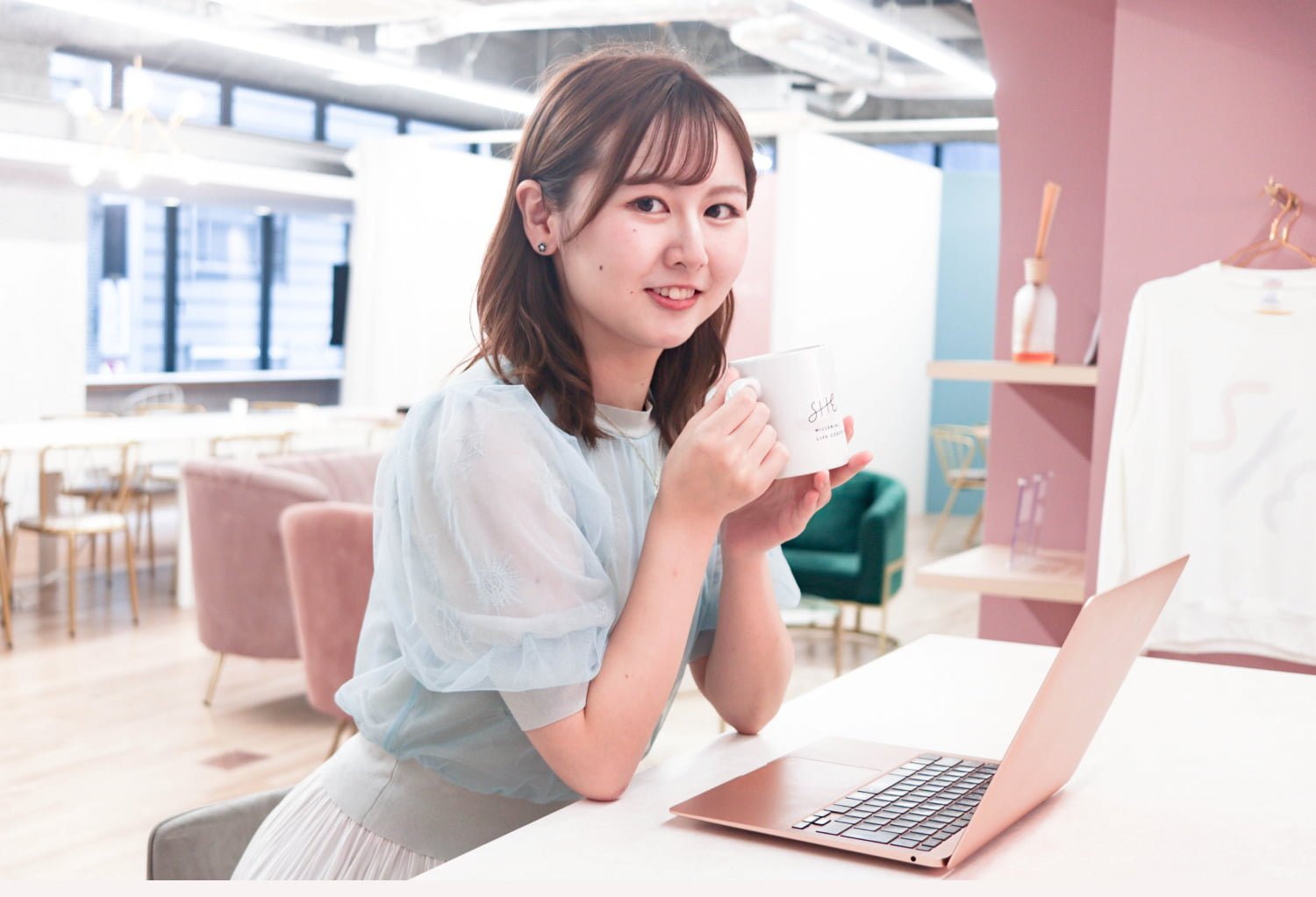 カフェのテーブルでマグカップを両手で持ち微笑む琴弓さん