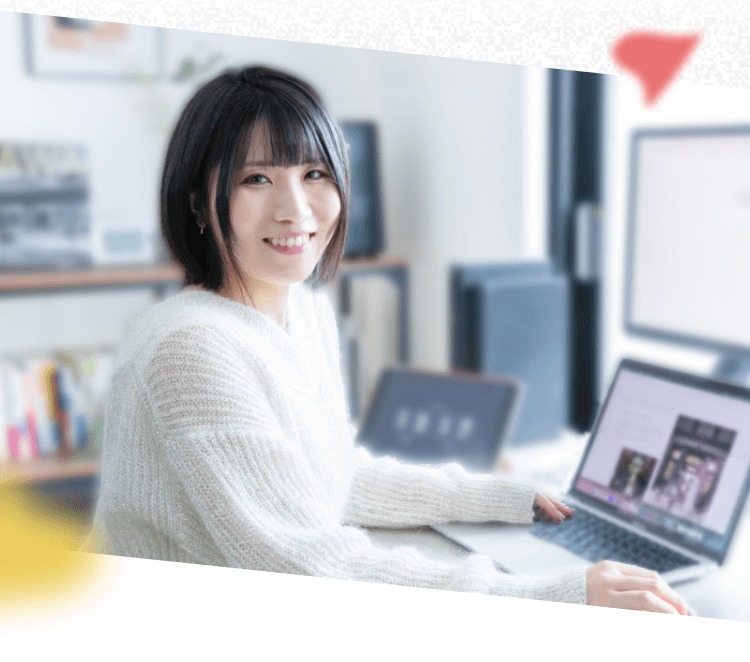 自宅デスクでノートPCに向かい、カメラを見て微笑むTomoyoさんの写真