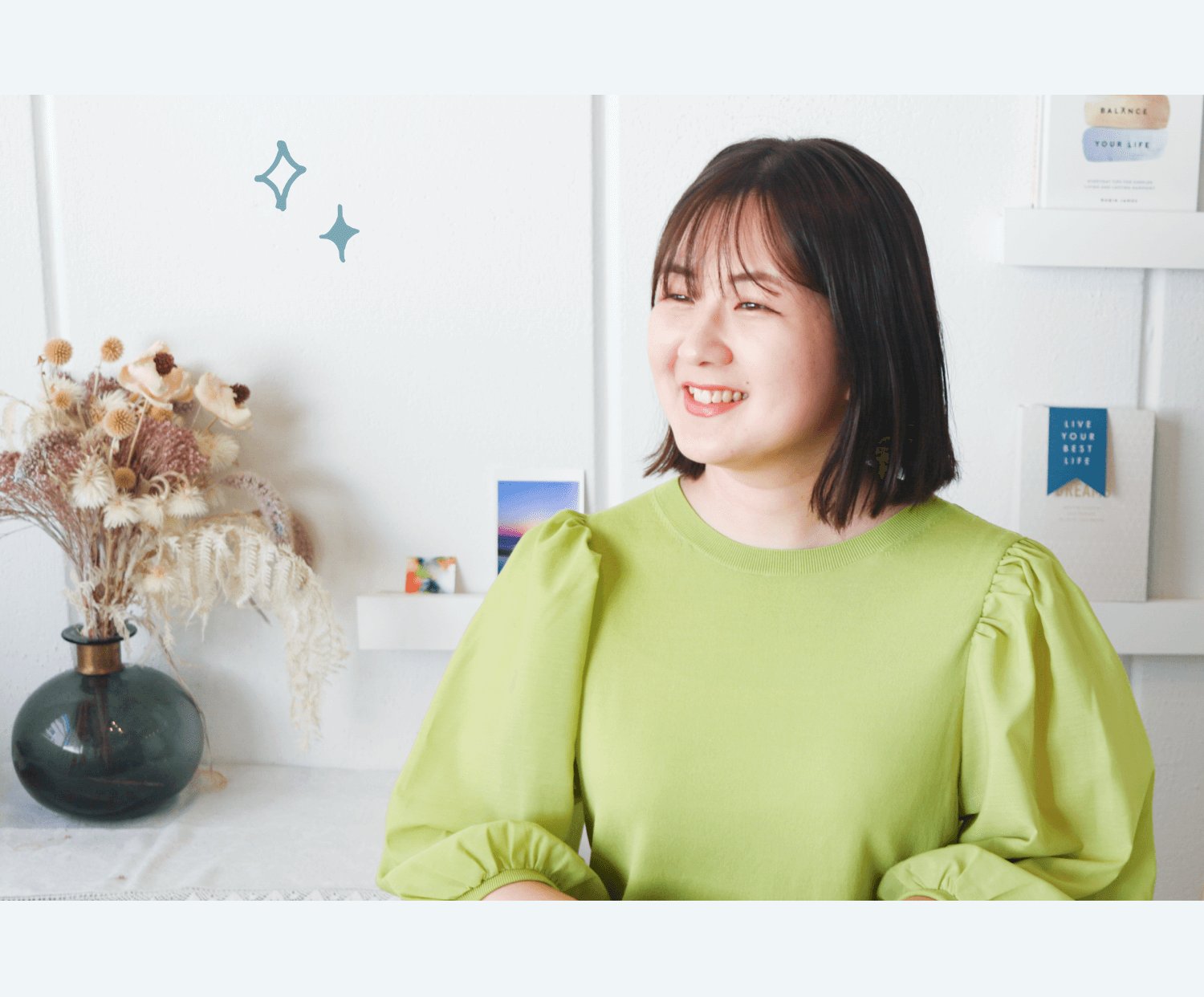 花瓶とドライフラワーが置かれた白い部屋で、微笑みながら斜め上を見る美咲さん