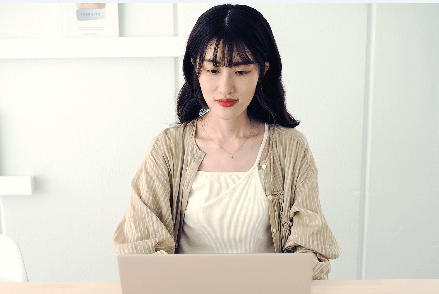 ノートパソコンに向かって作業するかえさん。ベージュのシャツに白いキャミソール姿