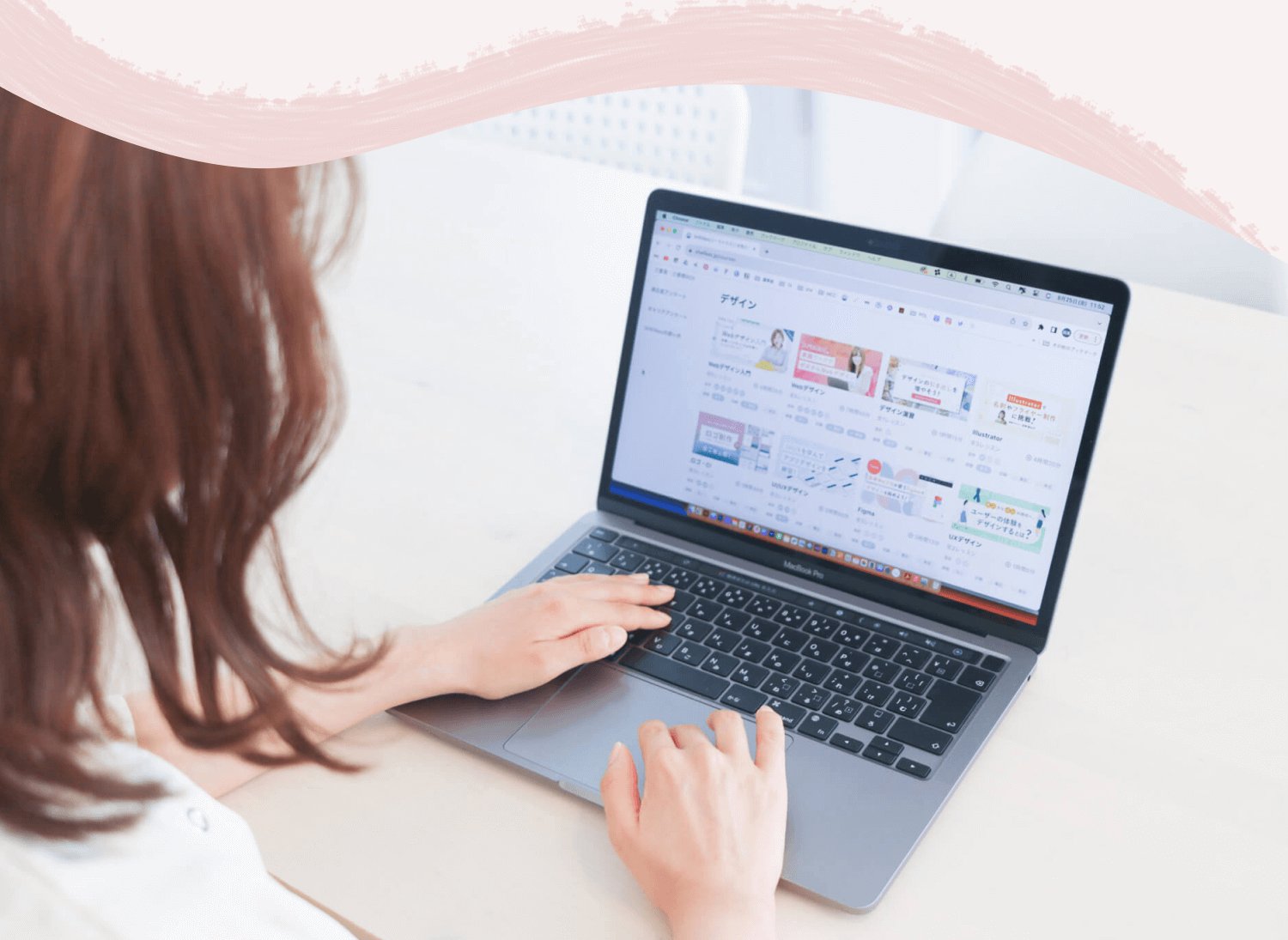 後ろ姿でノートPCのトラックパッド・キーボードを操作する手元。SHElikesのレッスン一覧画面が表示されている