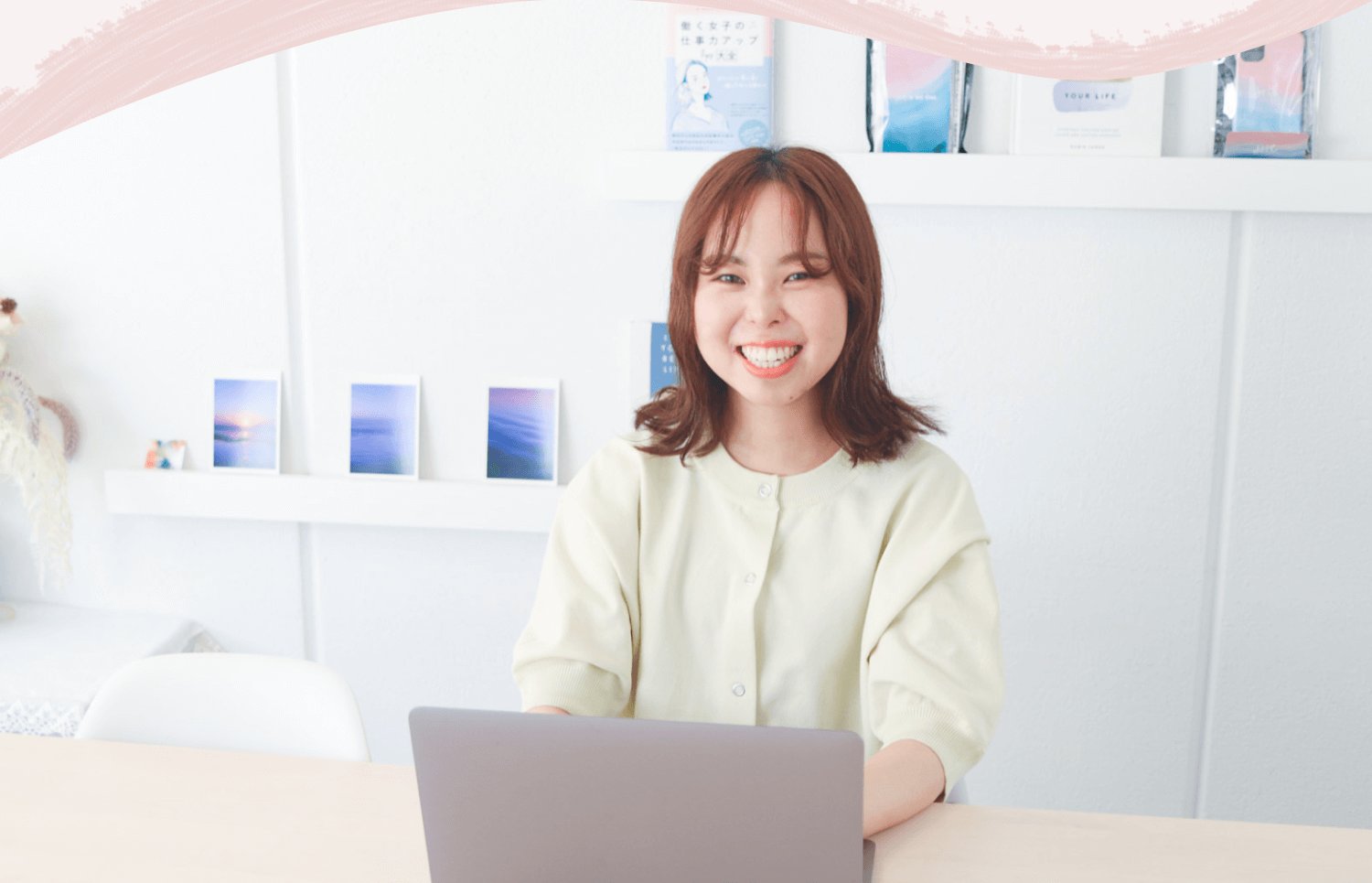 本棚を背景に、ノートPCを開いてデスクに向かい笑顔を見せる結風さんの正面ポートレート