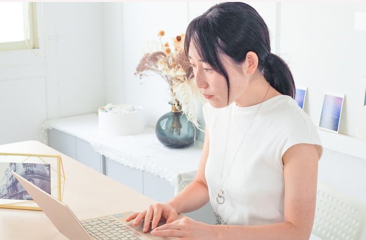 花瓶とドライフラワーのあるデスクでノートPCに向かうこじゆかさん