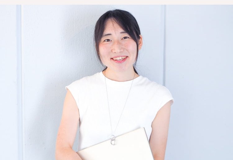 壁の前で書類を抱えて微笑むこじゆかさん