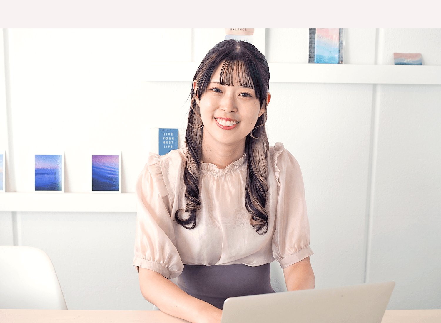 白い棚を背に、ノートパソコンを前にして微笑むすずかなさんのポートレート