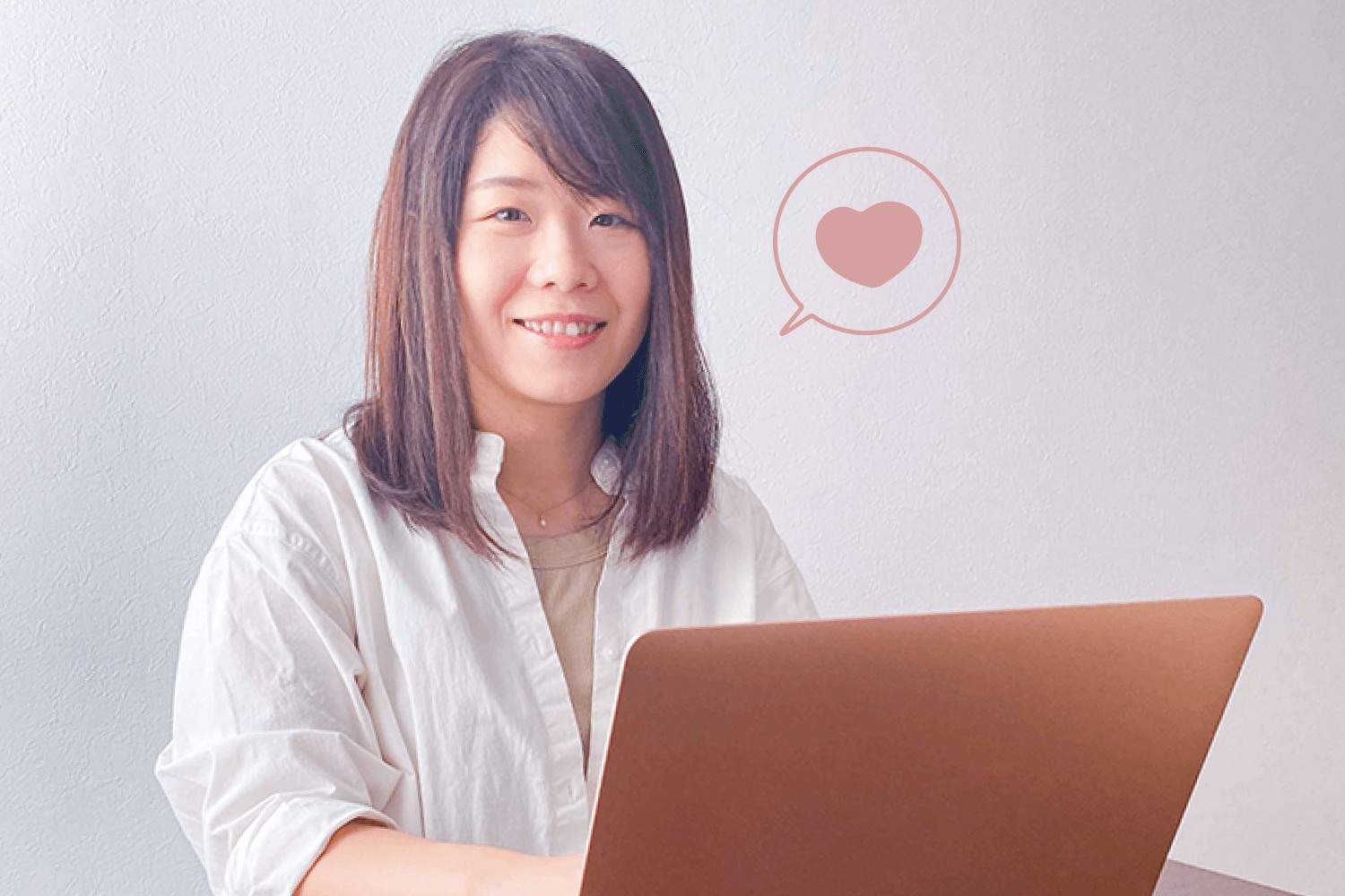 白シャツでノートPCに向かい微笑むゆみさん。ハート型の吹き出しアイコンの装飾つき