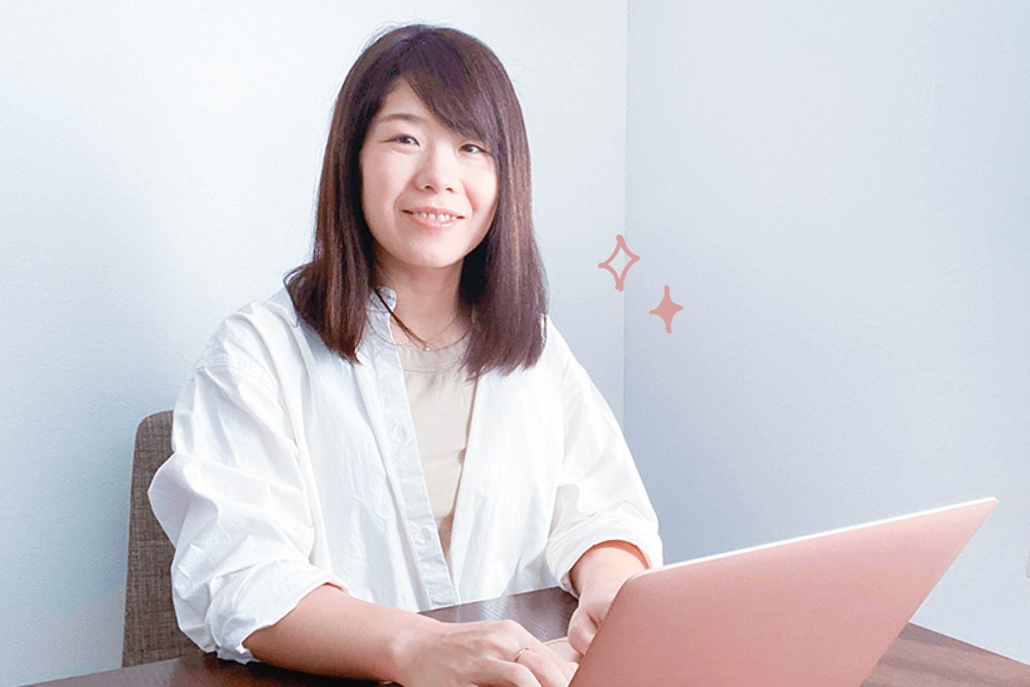 白シャツでピンク色のノートPCに向かい微笑むゆみさん