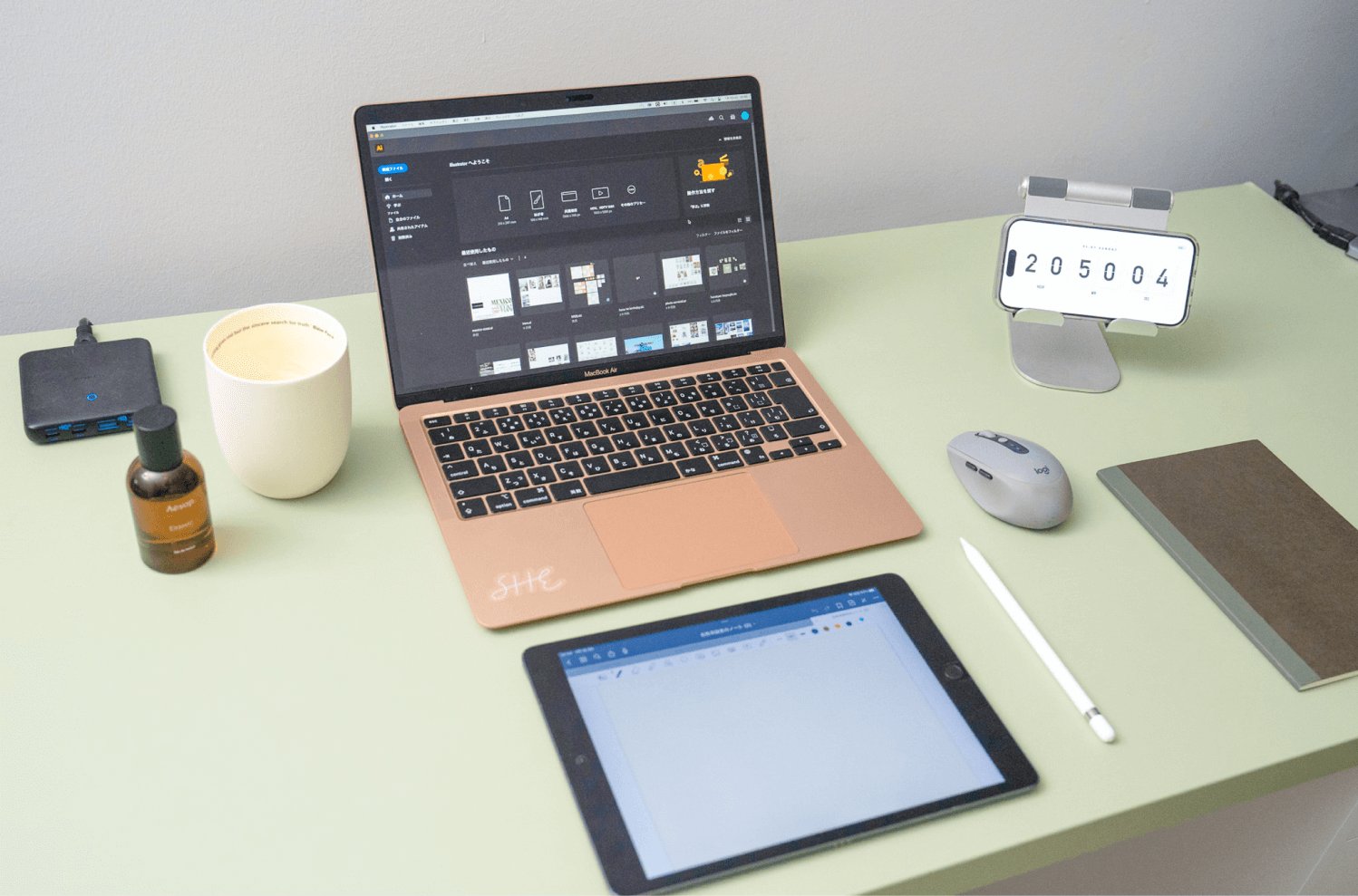 薄緑のデスクにMacBook・iPad・スマホスタンド・マウス・ノートなどが並ぶデスク周りのフラットレイ