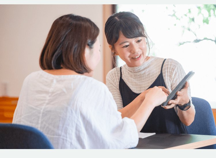 テーブルを挟んで対面で打ち合わせをするインタビュイー本人とクライアント。タブレットを操作しながら説明している