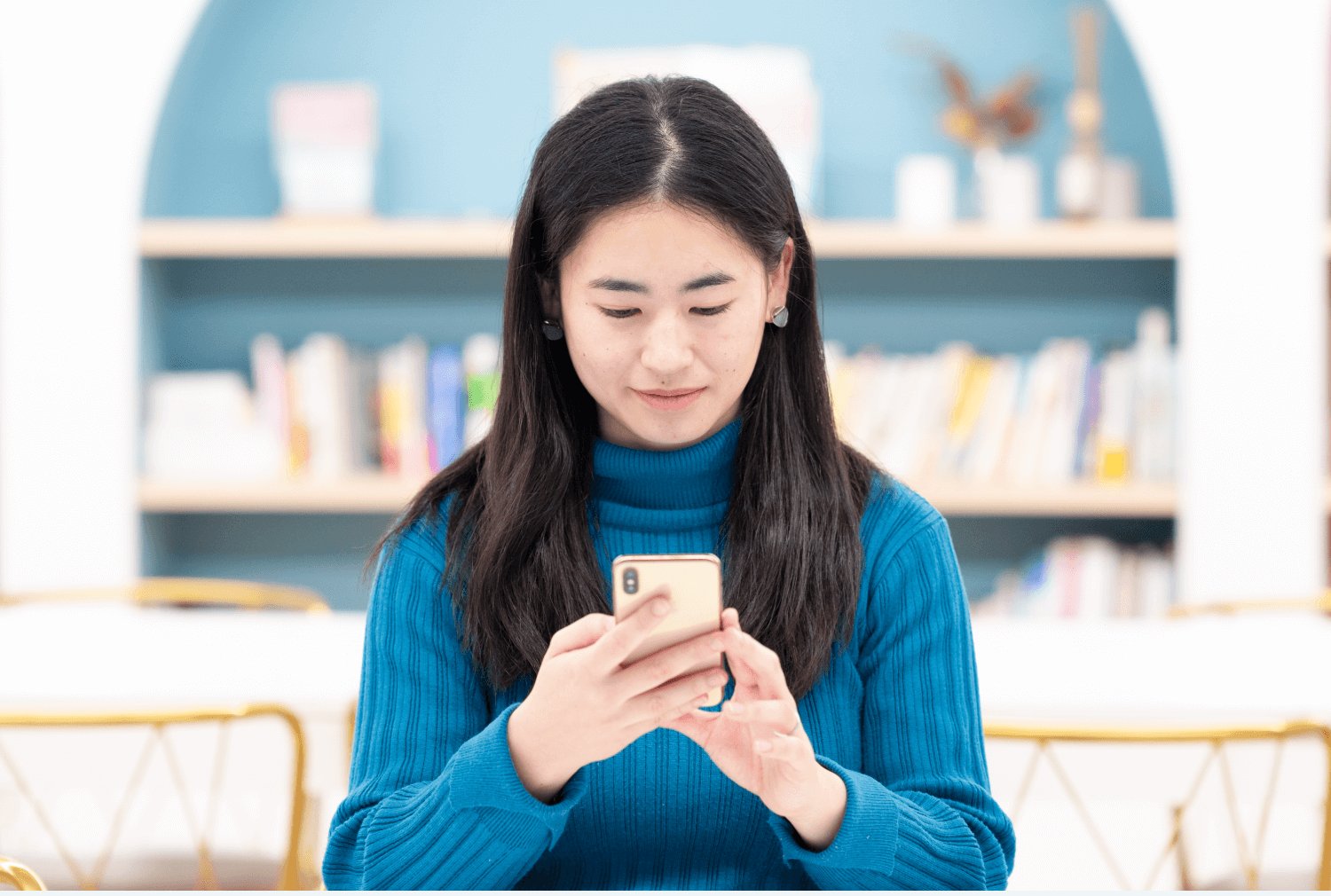 書棚を背に、青いニットで手にしたスマホを操作するぺっぱーさん