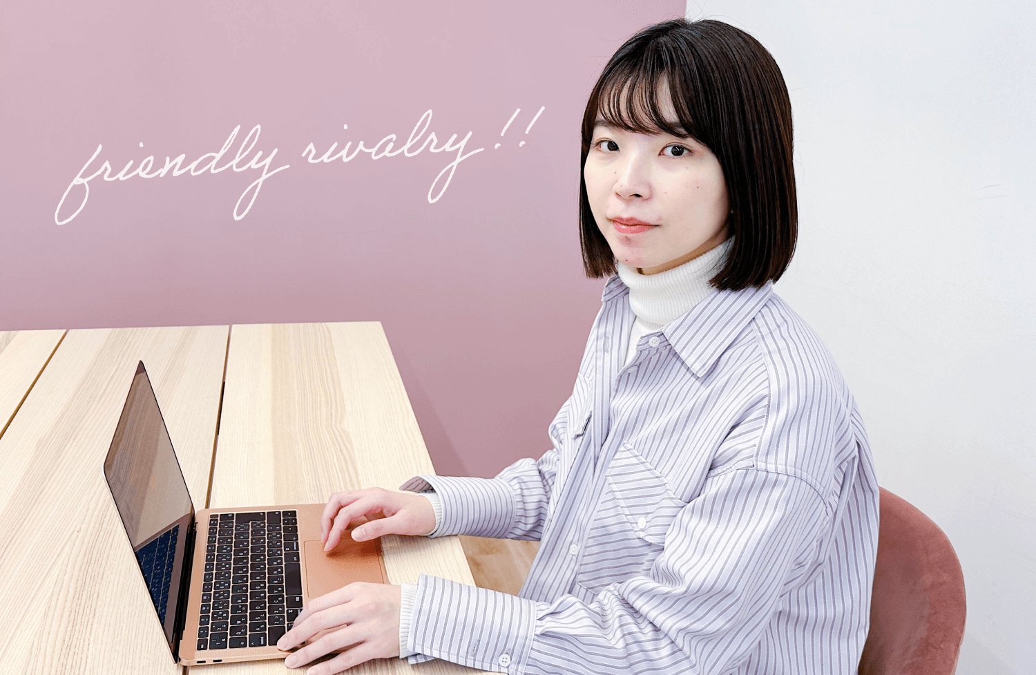 ピンク色の壁に「friendly rivalry!!」の装飾がある部屋で、ノートPCを操作しながらこちらを見る千晴さん