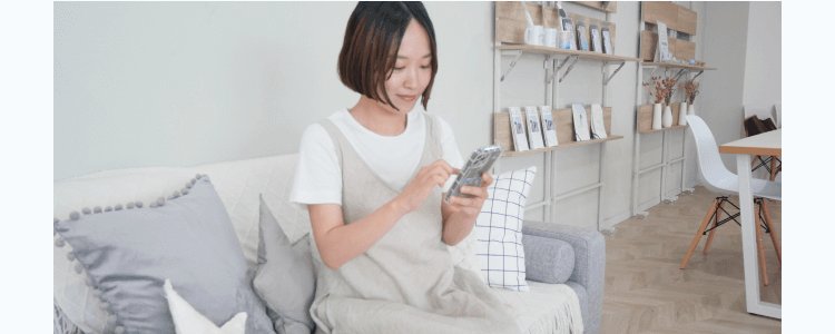 自宅のリビングでスマートフォンを操作しながら微笑むいおはるさん