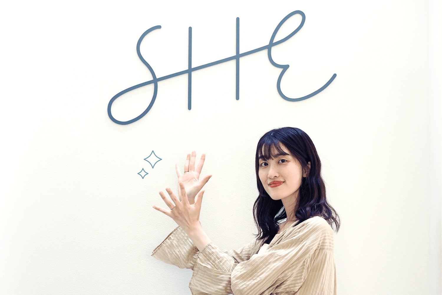 SHEのロゴの前で手を振るかえさんの写真