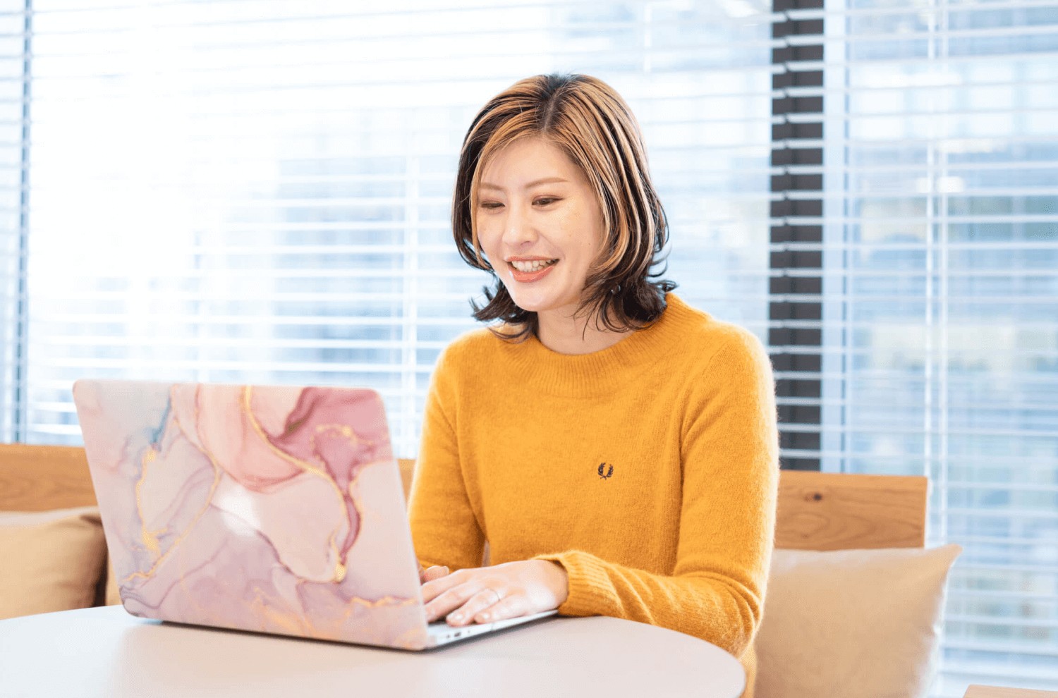 大理石柄ノートPCで作業するhaluさん。窓際・ブラインド越しの室内