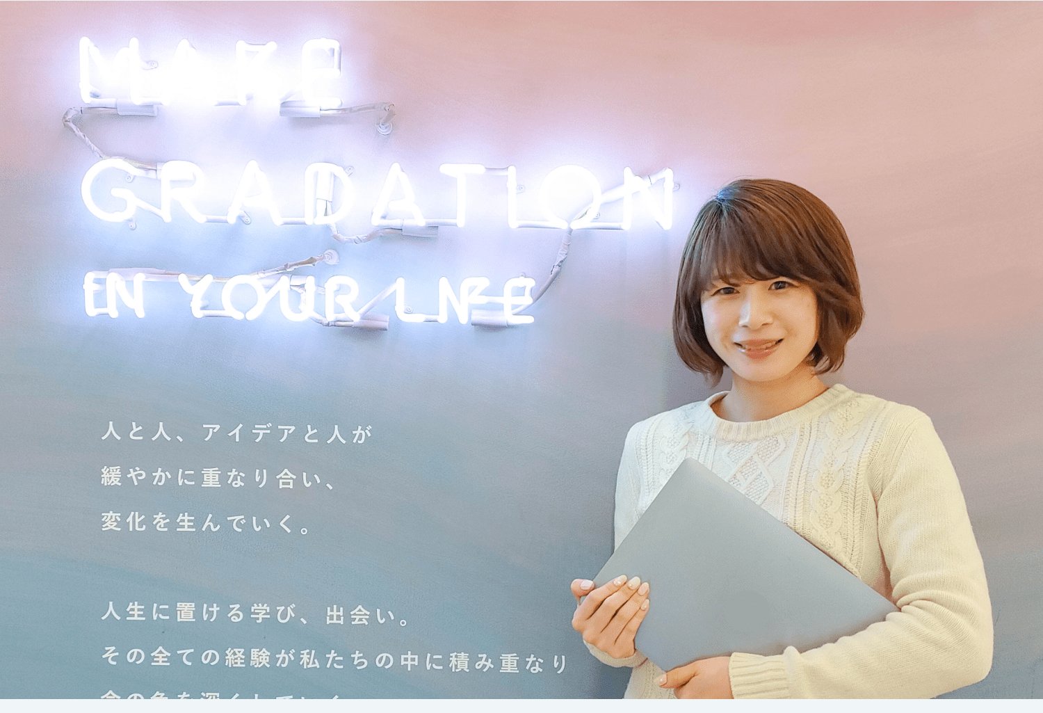 MAKE GRADATION IN YOUR LIFEというネオンサインの前でノートPCを抱えて微笑むぴょすさん