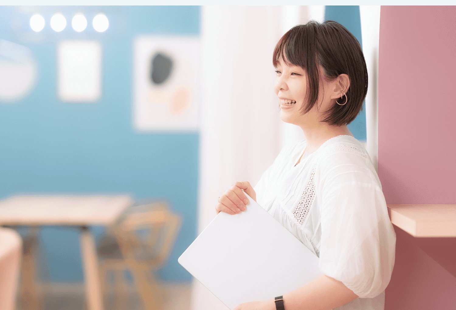 壁にもたれてノートPCを抱え、微笑むのりさんの横顔ポートレート