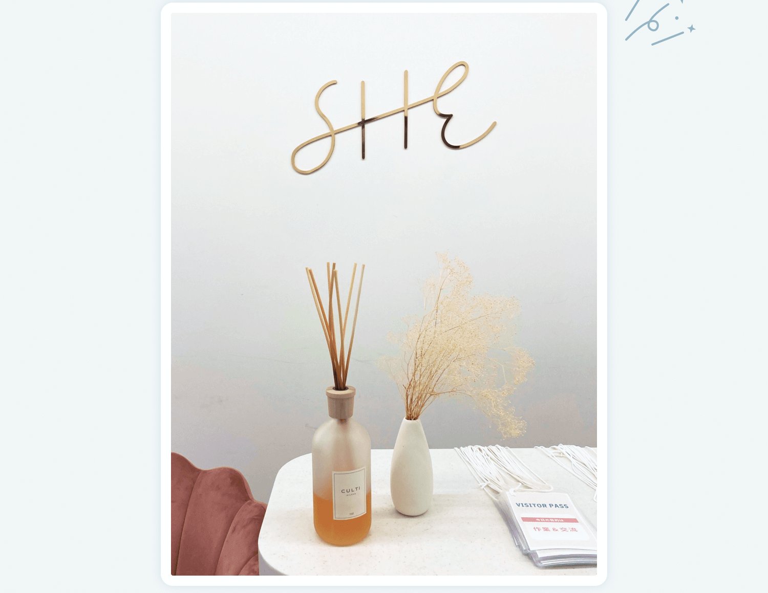 「SHE」のワイヤーオブジェの置物と、リードディフューザー・ドライフラワー・「VISITOR PASS」の来訪証が置かれた丸テーブル