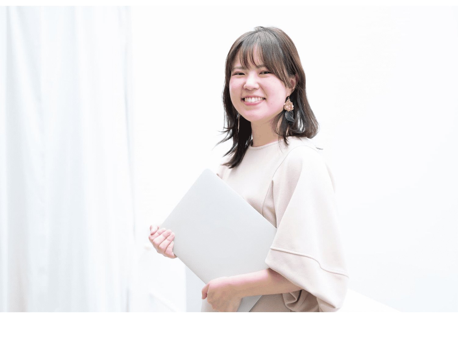 白いカーテンを背景にノートPCを抱えて微笑むさやかさん
