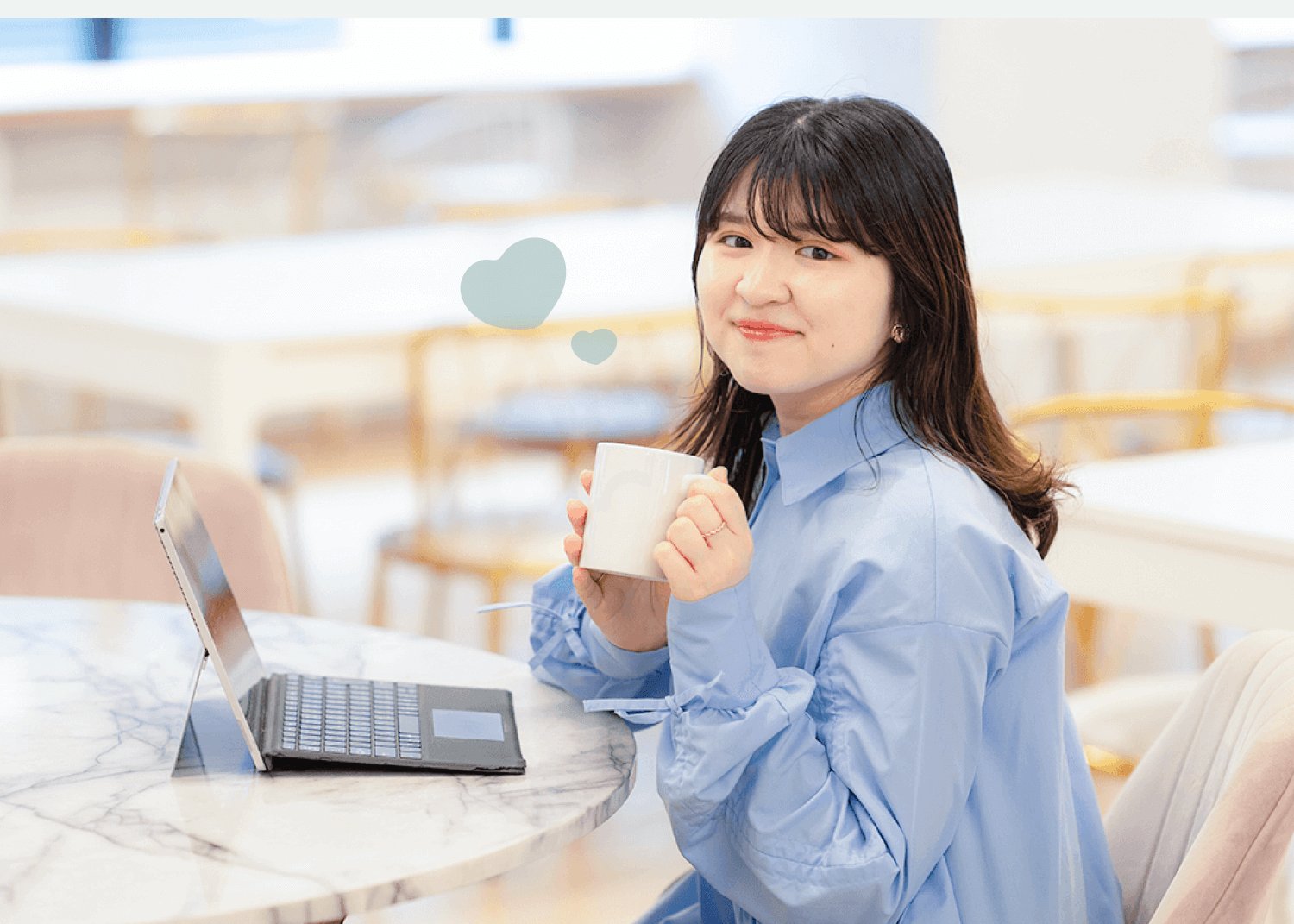 カフェのテーブルでノートPCとマグカップを手に振り返るこじはるさん