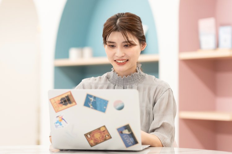 棚に囲まれた店内で、ステッカーを貼ったノートPCに向かい微笑むさくらさんの写真